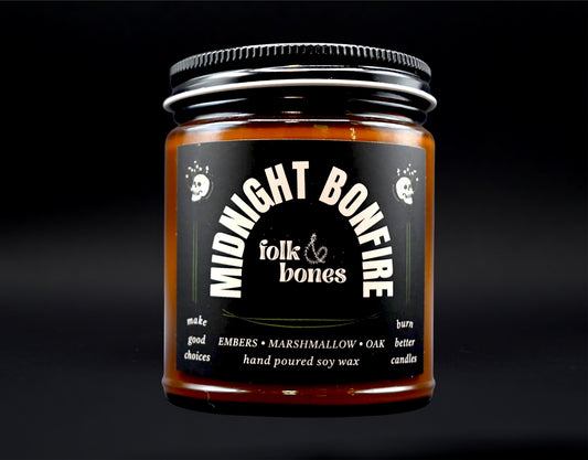 Folk and Bones Midnight Bonfire 8 oz soy candle in a glass jar with a black lid, showing the candle's dark wax and wooden wick.