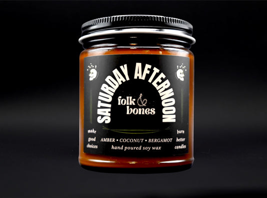 Folk and Bones Saturday Afternoon 8 oz soy candle in a glass jar with a natural wooden lid and a cozy, softly glowing wick.