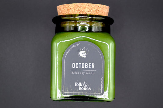 Folk and Bones October 8 oz soy candle in a glass jar with an autumn-inspired label and warm, inviting glow.