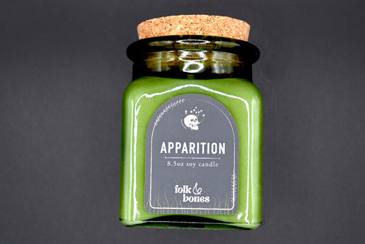 Folk and Bones Apparition 8 oz soy candle in a glass jar with a white label and wooden wick, ready for cozy ambiance.