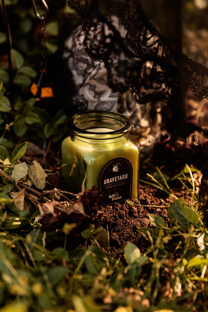 Folk and Bones Graveyard 8 oz soy candle with dark label and lid, ideal for gothic or spooky decor.