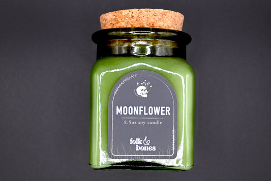 Folk and Bones Moonflower 8 oz soy candle in a glass jar with a lit wick, decorative label, and floral moonflower design.