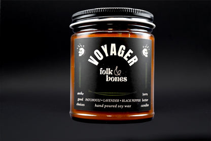 Folk and Bones Voyager 8 oz soy candle in a glass jar with a lit wick and minimalist label on a neutral background.