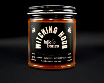 Folk and Bones Witching Hour 8oz soy candle in a dark jar with a black lid, featuring a mystical label design.