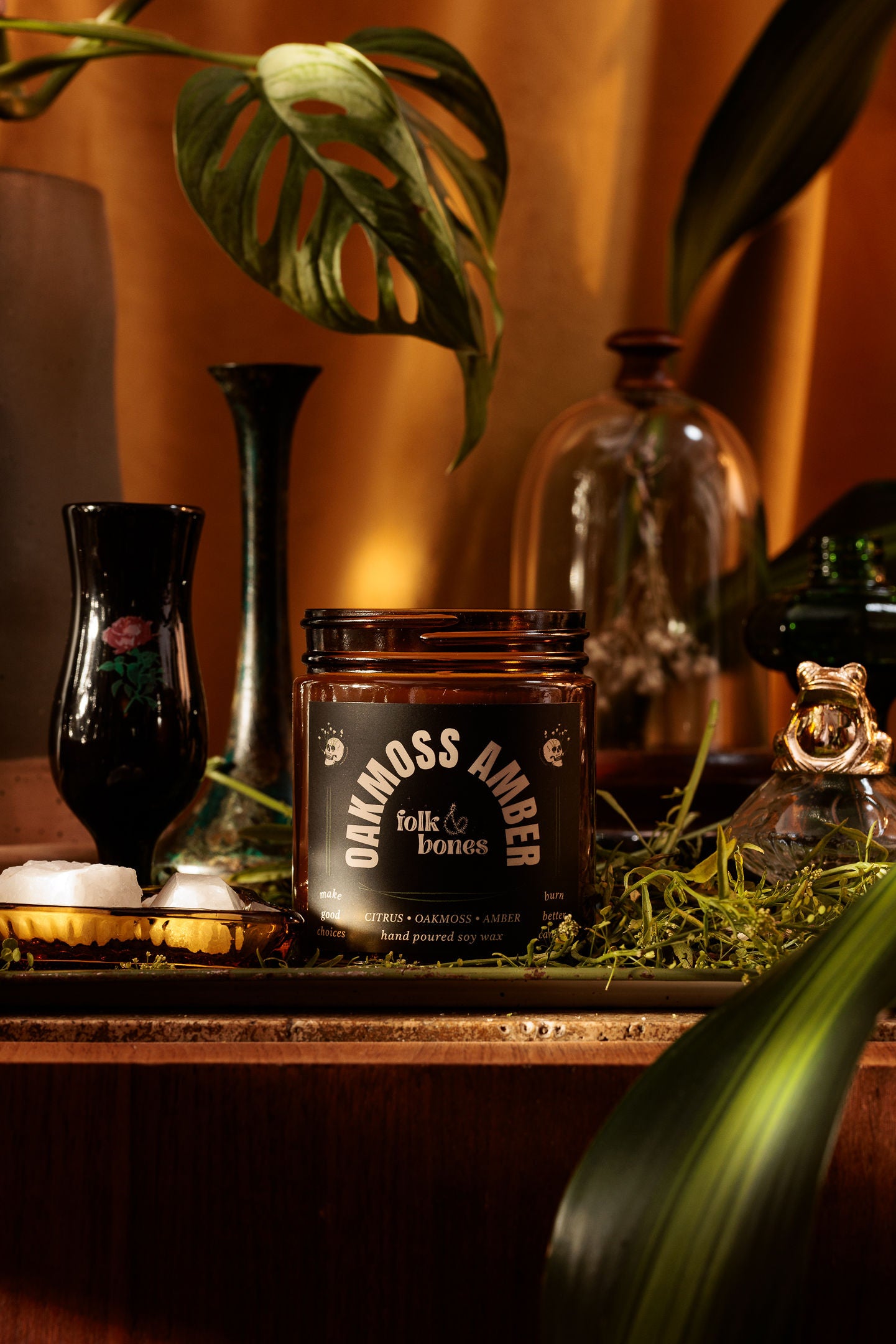 Folk and Bones Oakmoss Amber soy candle in an 8 oz glass jar, featuring a natural wax finish and a lit wick for cozy ambiance.